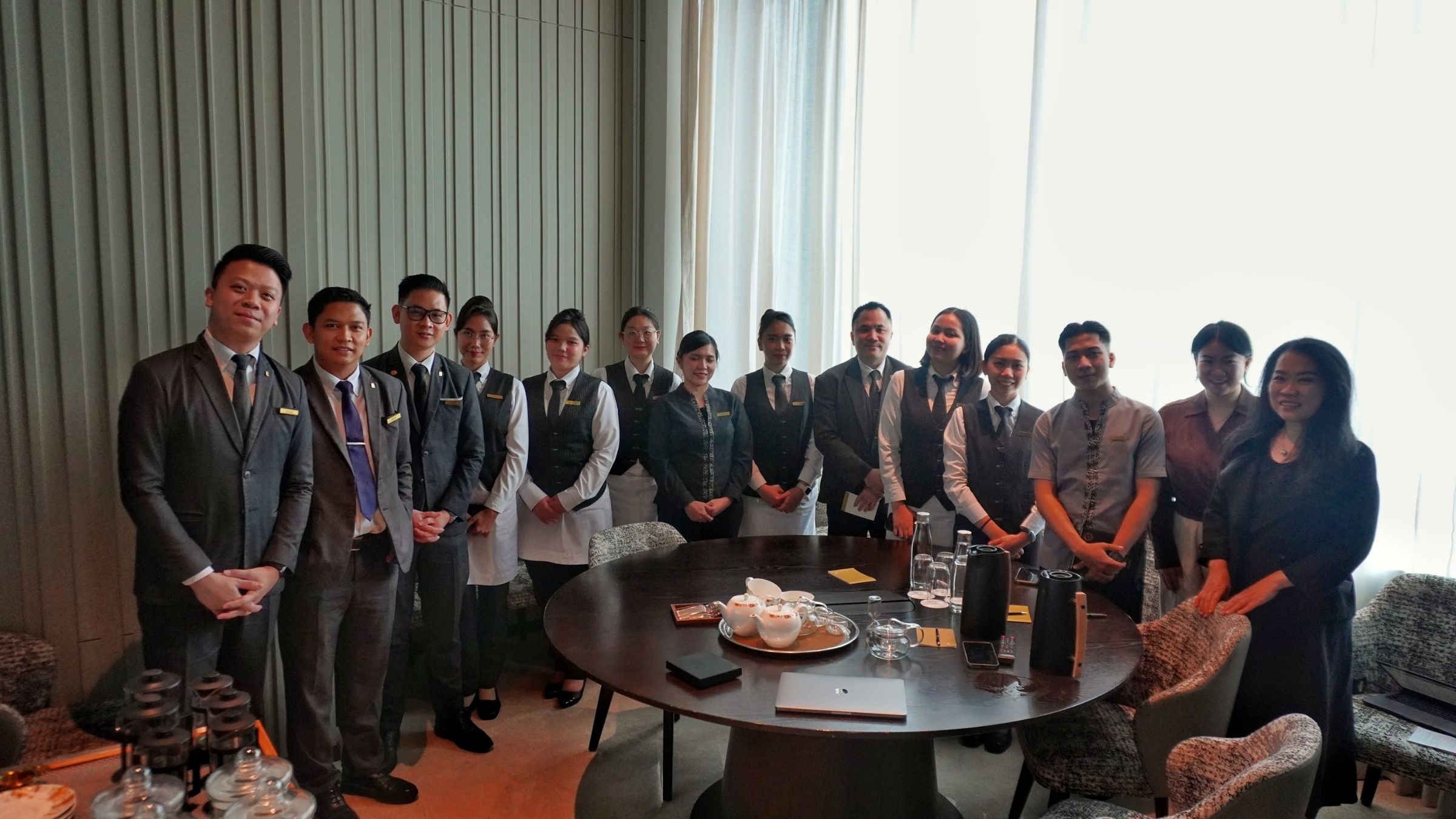 A hotel service team standing around a table set with teapots, cups and glass teaware